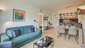 A modern living room with a teal sofa, a dining table with chairs, and a kitchen area with wooden cabinets and a hanging light fixture. - Porto Letizia P5, Porlezza, Italy (Porlezza)
