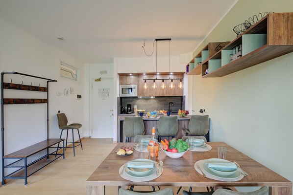 A modern kitchen with a built-in microwave, wooden shelves, and a dining area with a wooden table set for four. - Porto Letizia P5, Porlezza, Italy (Porlezza)