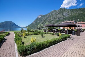 A paved walkway with a well-maintained garden and outdoor seating area, overlooking a body of water and mountains. - Porto Letizia S14 B1, Porlezza, Italy (Porlezza)