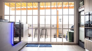 A modern kitchen with a large sliding glass door leading to a balcony, a refrigerator, and a countertop with a sink. - TOUR INN (Malé)