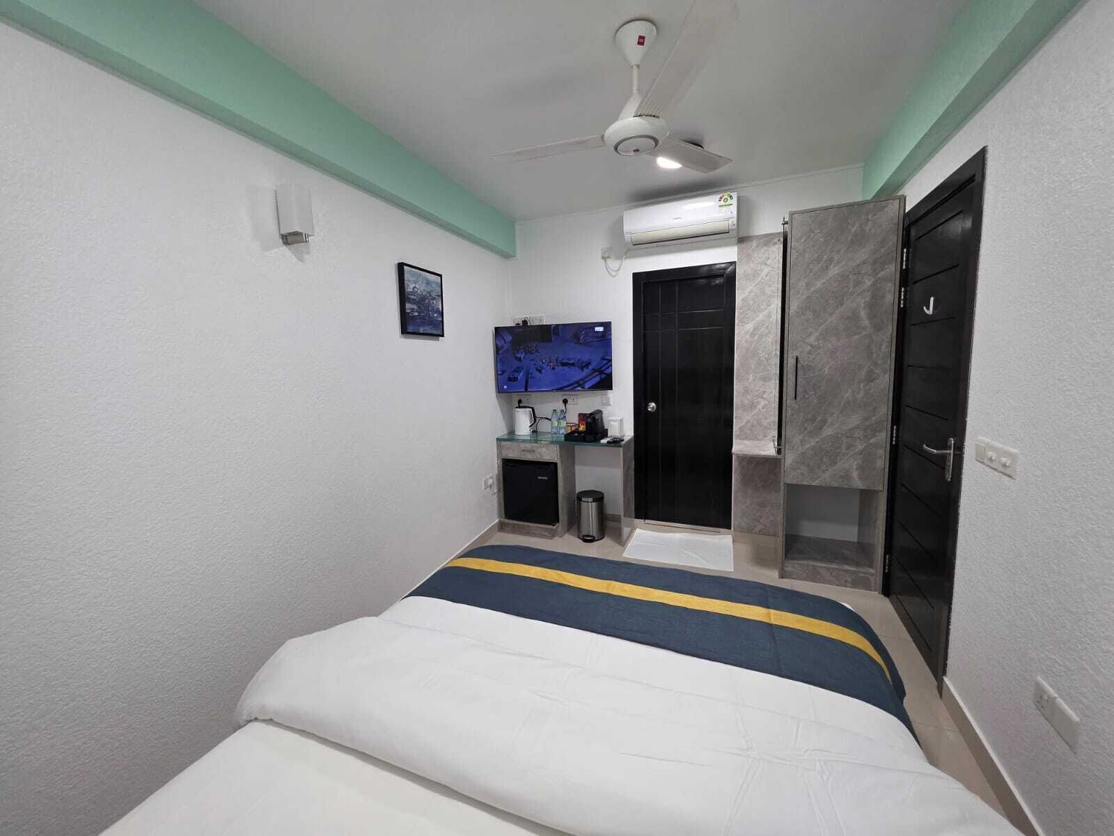 Un dormitorio con cama, ventilador de techo, televisión, una puerta y una pequeña zona de kitchenette.