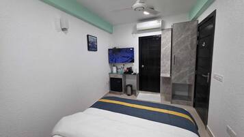 Un dormitorio con cama, ventilador de techo, televisión, una puerta y una pequeña zona de kitchenette.