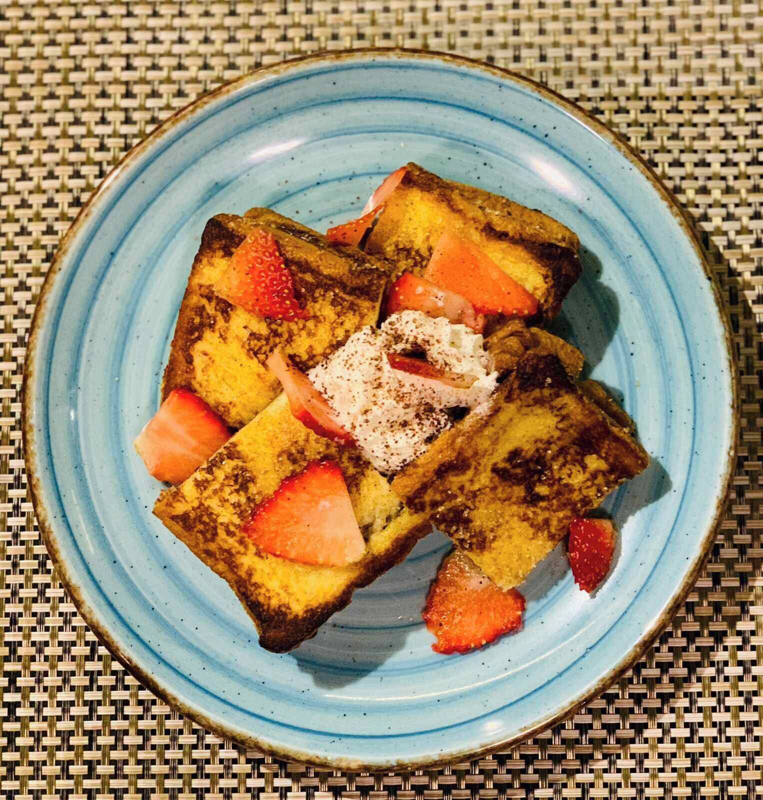 A plate of French toast with strawberries and powdered sugar on a blue plate.