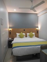 Una habitación de hotel con una cama, lámparas de noche, ventilador de techo y luz empotrada.