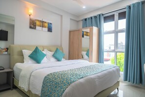 Una habitación de hotel con cama, armario, televisor y ventana con cortinas.