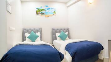 A hotel room with two beds, each with a tufted headboard and blue bedding. There is a wall-mounted artwork depicting a beach scene.