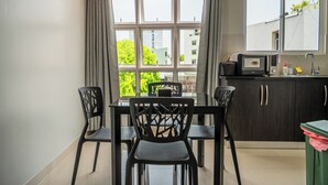 A dining area with a table and chairs, a window with curtains, a microwave, and a trash bin. - TOUR INN (Malé)