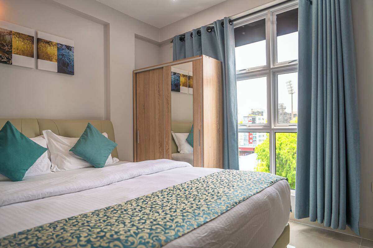Ein Hotelzimmer mit Bett, Kleiderschrank und einem großen Fenster mit Vorhängen.