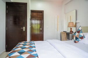 Una habitación de hotel con una cama, una puerta de madera, un escritorio con lámpara y un espejo.