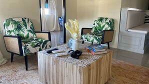 A room with two chairs with a tropical leaf pattern, a wooden coffee table with books and a vase, and a view of a balcony with a railing. - A taste of paradise, luxury villa on the beautiful Northern Coast! (Florence Hall Village)