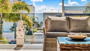 A balcony with a wicker sofa, a small table, and a decorative stone sculpture.