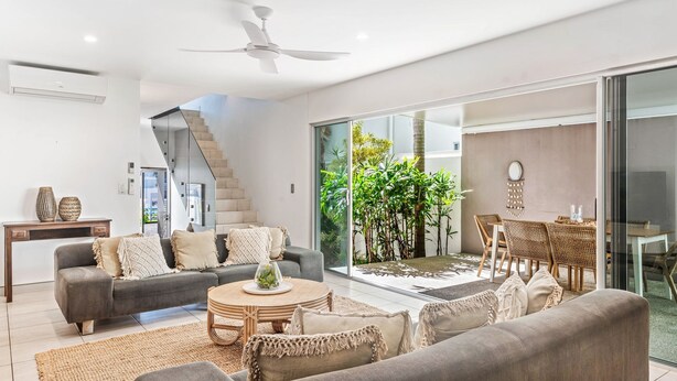 A modern living room with a grey sofa, a round coffee table, and a dining area with wicker furniture.