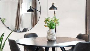 Une table de salle à manger ronde avec des chaises, un vase de fleurs, un miroir rond et un lampadaire.