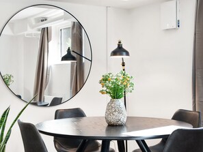 Une table de salle à manger ronde avec des chaises, un vase de fleurs, un miroir rond et un lampadaire.