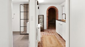 Une cuisine avec des meubles blancs, une arche en briques et un sol carrelé.