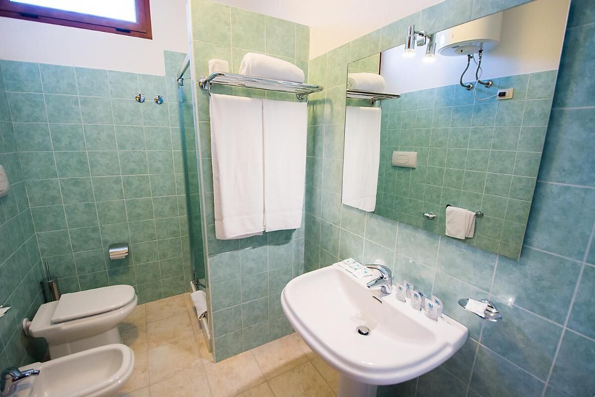 A bathroom with a toilet, bidet, sink, and a shower area.