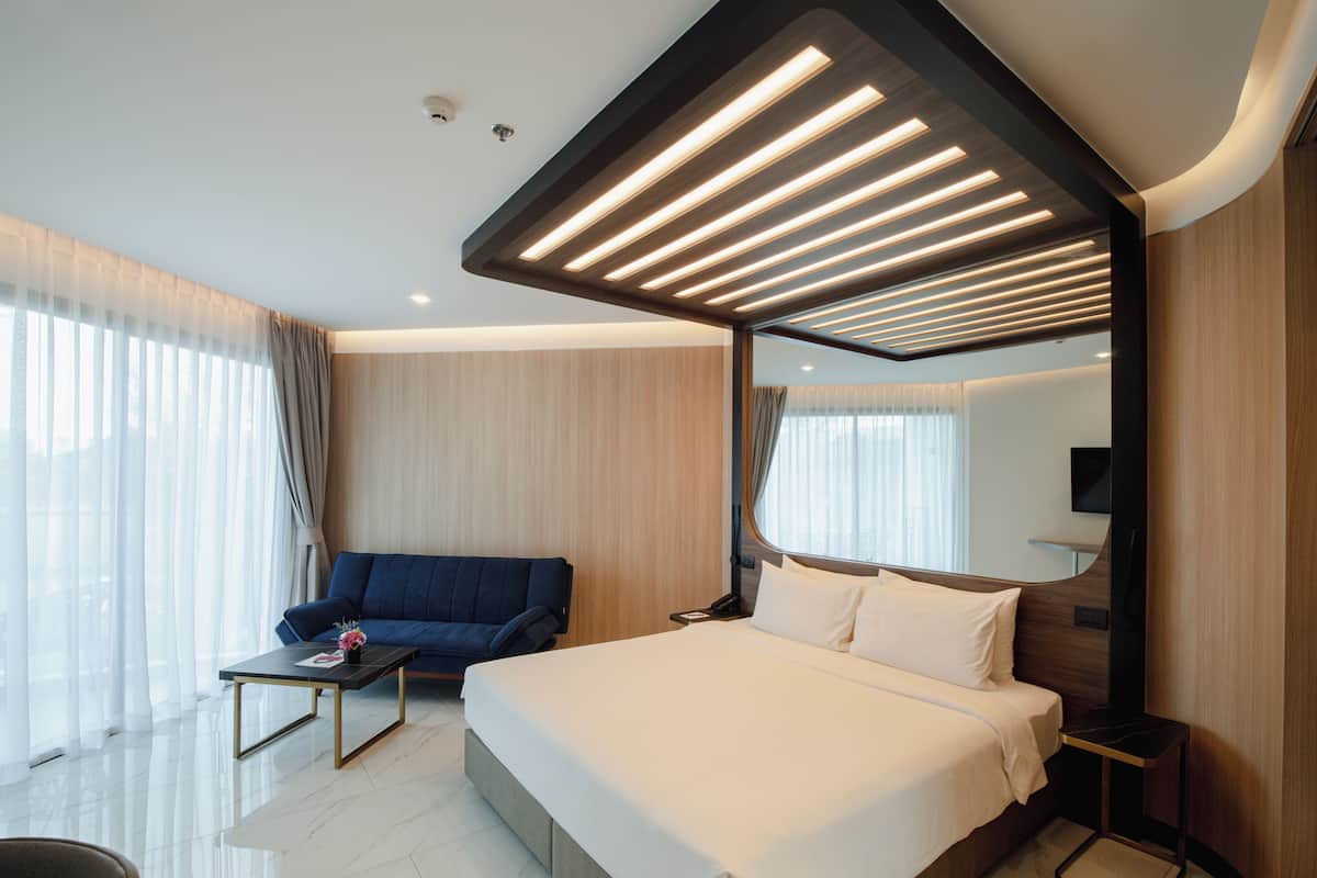 Une chambre d’hôtel moderne avec un grand lit, un canapé, une petite table et un grand miroir.
