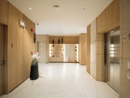 Un vestíbulo de hotel moderno con paneles de madera, suelo de mármol, mostrador de recepción y un ascensor.