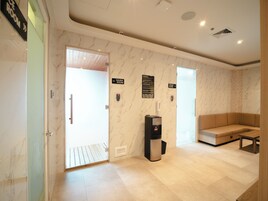 Un vestíbulo moderno con suelo de mármol, dispensador de agua, un sofá y señalización para sauna y baño de vapor.