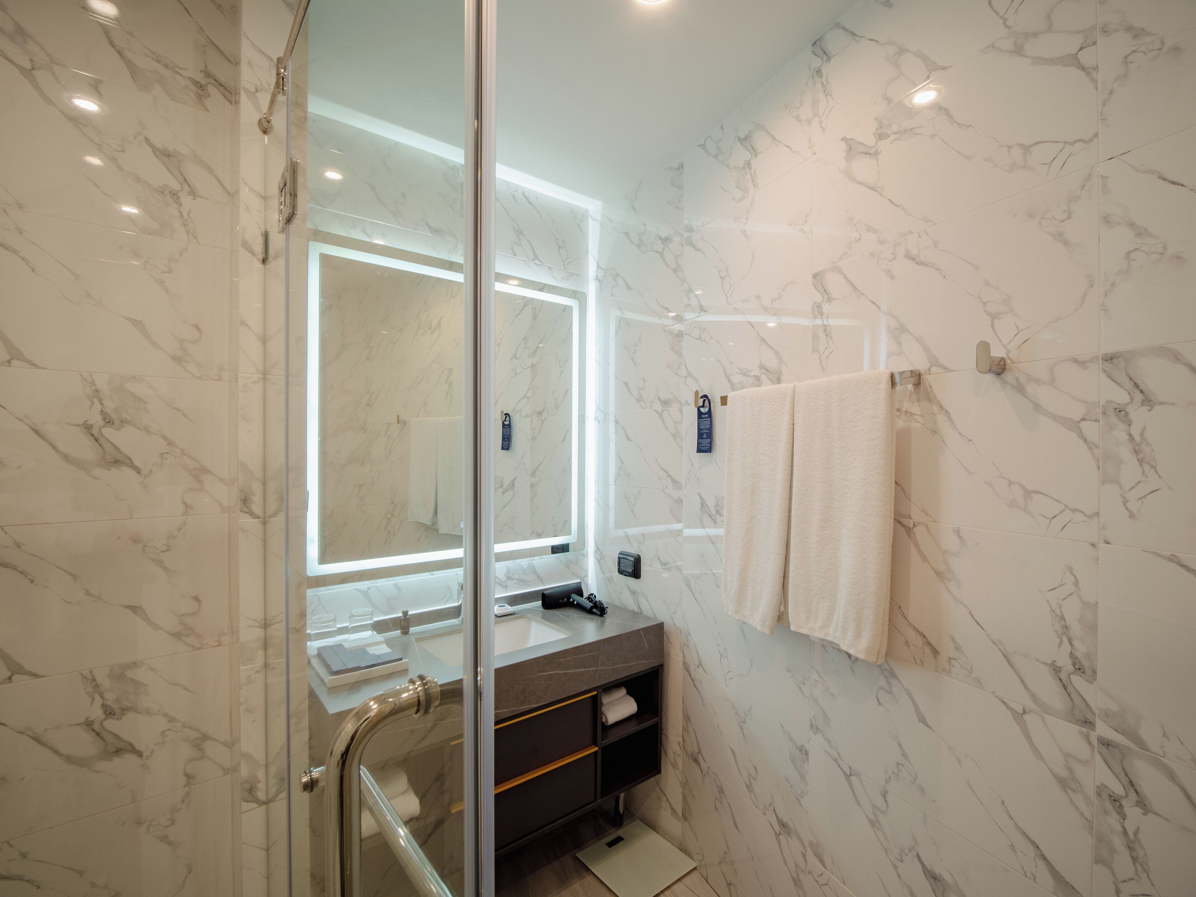 A modern bathroom with marble walls, a glass shower enclosure, a vanity with a mirror, and a towel rack.