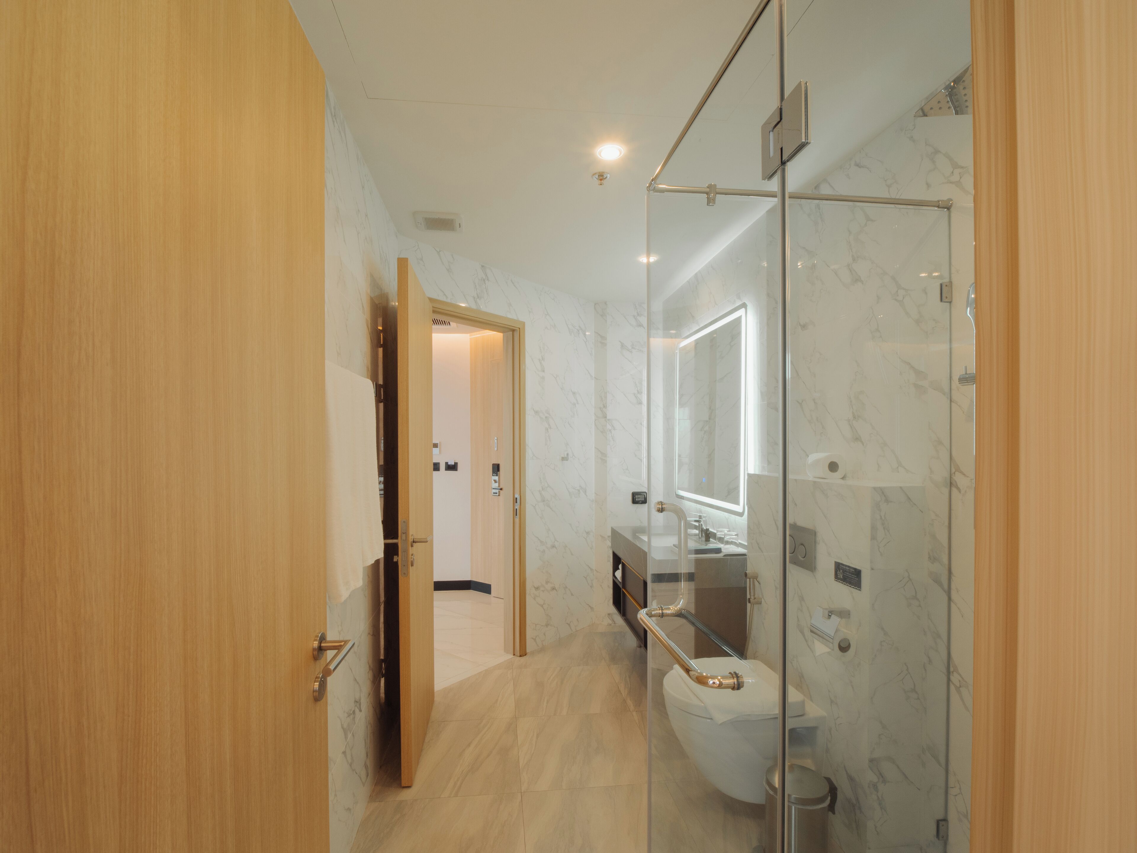 A modern bathroom with a glass-enclosed shower, a marble-tiled floor, and a wooden door.