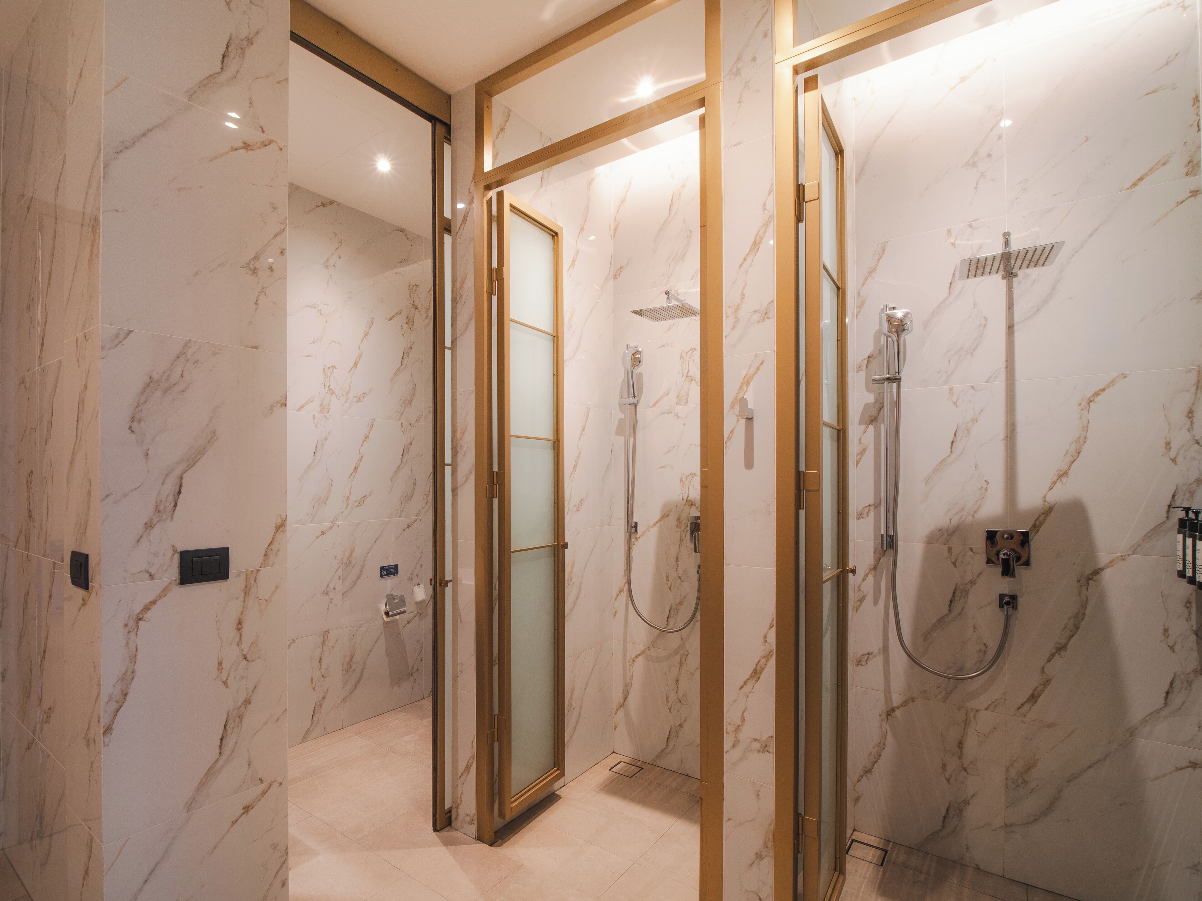 A modern bathroom with marble walls, a glass-enclosed shower, and a gold-framed mirror.