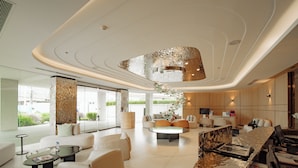 Un hall d’hôtel moderne doté d’un plafond incurvé, d’un espace détente avec des canapés et des fauteuils, d’un comptoir d’accueil et d’une grande fenêtre offrant une vue sur la verdure.