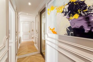 Un couloir avec une grande peinture abstraite au mur, un plancher en bois et des portes blanches dotées de poignées dorées.