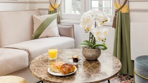 Una mesa redonda de mármol con alimentos para el desayuno, una orquídea en maceta y vistas a una ventana con cortinas.