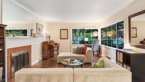 A living room with a fireplace, a sofa, a coffee table, and a large window with a view of trees. - Perch - Wedgwood Haven: Spacious | Office | Family-Friendly (Seattle)