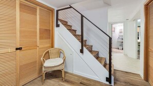 A staircase with wooden steps and a metal railing, leading to a room with a wicker chair and a wooden door. - Perch - Wedgwood Haven: Spacious | Office | Family-Friendly (Seattle)