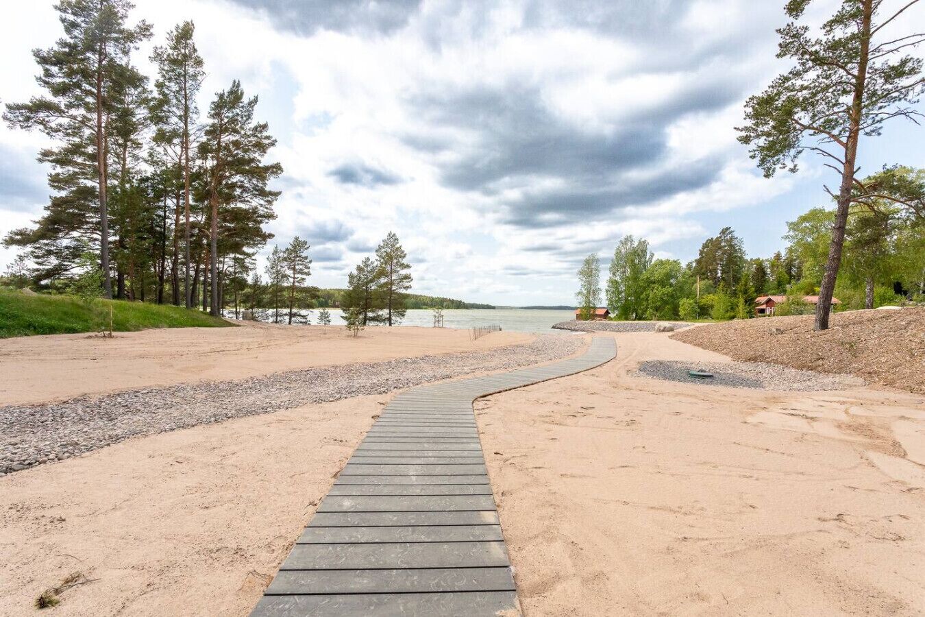 A wooden boardwalk leading to a sandy beach with a lake and trees in the background.