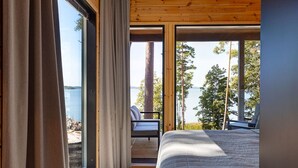 A bedroom with a large bed, a view of the lake, and a deck area with a chair.