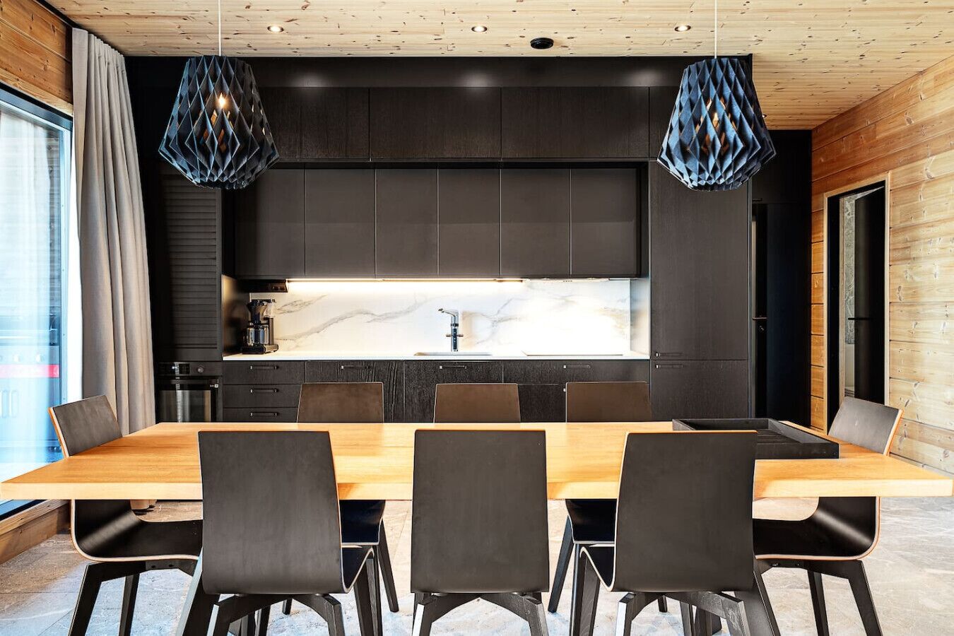 A modern kitchen with dark cabinetry, a marble countertop, and pendant lighting.