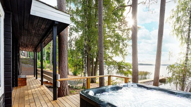 A wooden deck with a hot tub, surrounded by trees and overlooking a body of water.