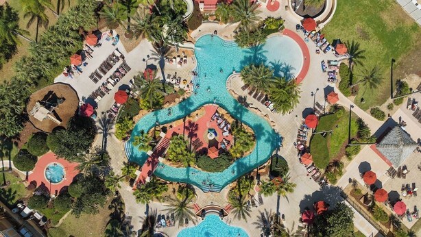 An aerial view of a resort with multiple swimming pools, palm trees, and outdoor seating areas. - Hogwarts Express House at Regal Palms Resort | Sage Vacations (Davenport)