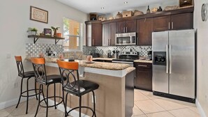 A modern kitchen with dark wooden cabinets, stainless steel appliances, a granite countertop, and a bar area with stools. - Hogwarts Express House at Regal Palms Resort | Sage Vacations (Davenport)