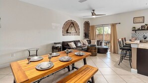 A dining area with a wooden table set for four, a sofa, and a kitchen area with a bar. - Hogwarts Express House at Regal Palms Resort | Sage Vacations (Davenport)