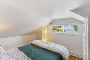 Ein Schlafzimmer mit Bett, Fenster mit Meerblick und schrägen Wänden.