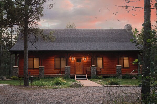 A log cabin with a stone foundation, a front porch with seating, and a driveway leading to the entrance.