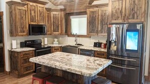 Eine Küche mit Holzausstattung, einer Arbeitsplatte aus Granit, einem Edelstahlkühlschrank und einer Mikrowelle.