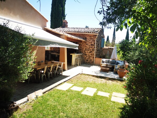 A patio with a stone wall, a dining table with chairs, a barbecue grill, and a small seating area.