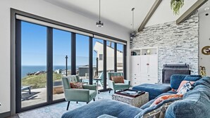 A modern living room with a large sliding glass door, a stone wall, and a fireplace. - Sweeping Ocean Views · Hot Tub · Fire Pit · Dillon Beach (Dillon Beach)