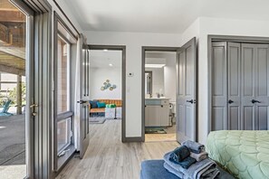 Ein Zimmer mit einem Bett, eine Sitzbank mit Handtüchern, ein Badezimmer mit Waschbecken und Spiegel sowie ein Flur, der zu einem weiteren Zimmer führt.