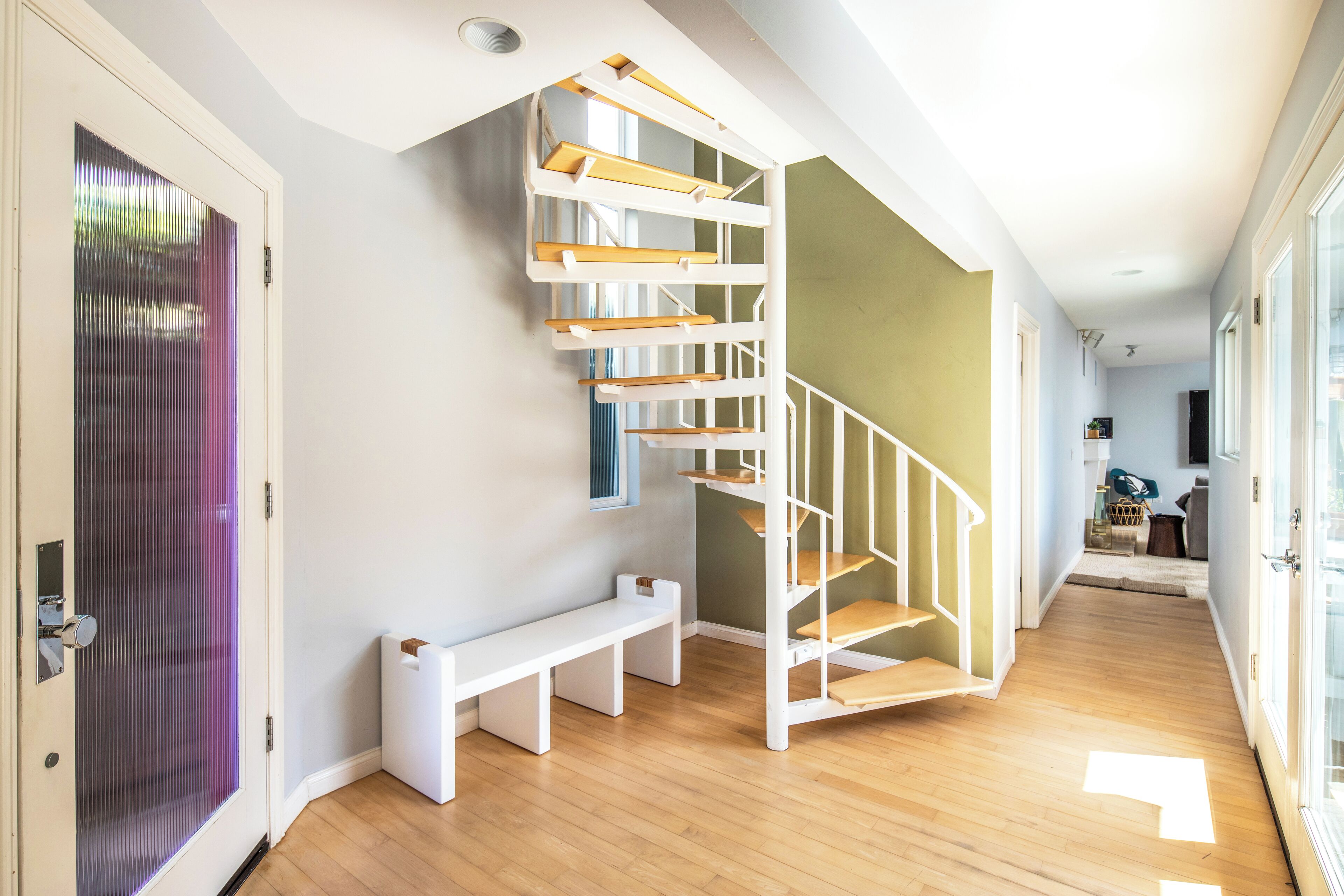 A modern interior with a wooden staircase, a bench, and a door with frosted glass.