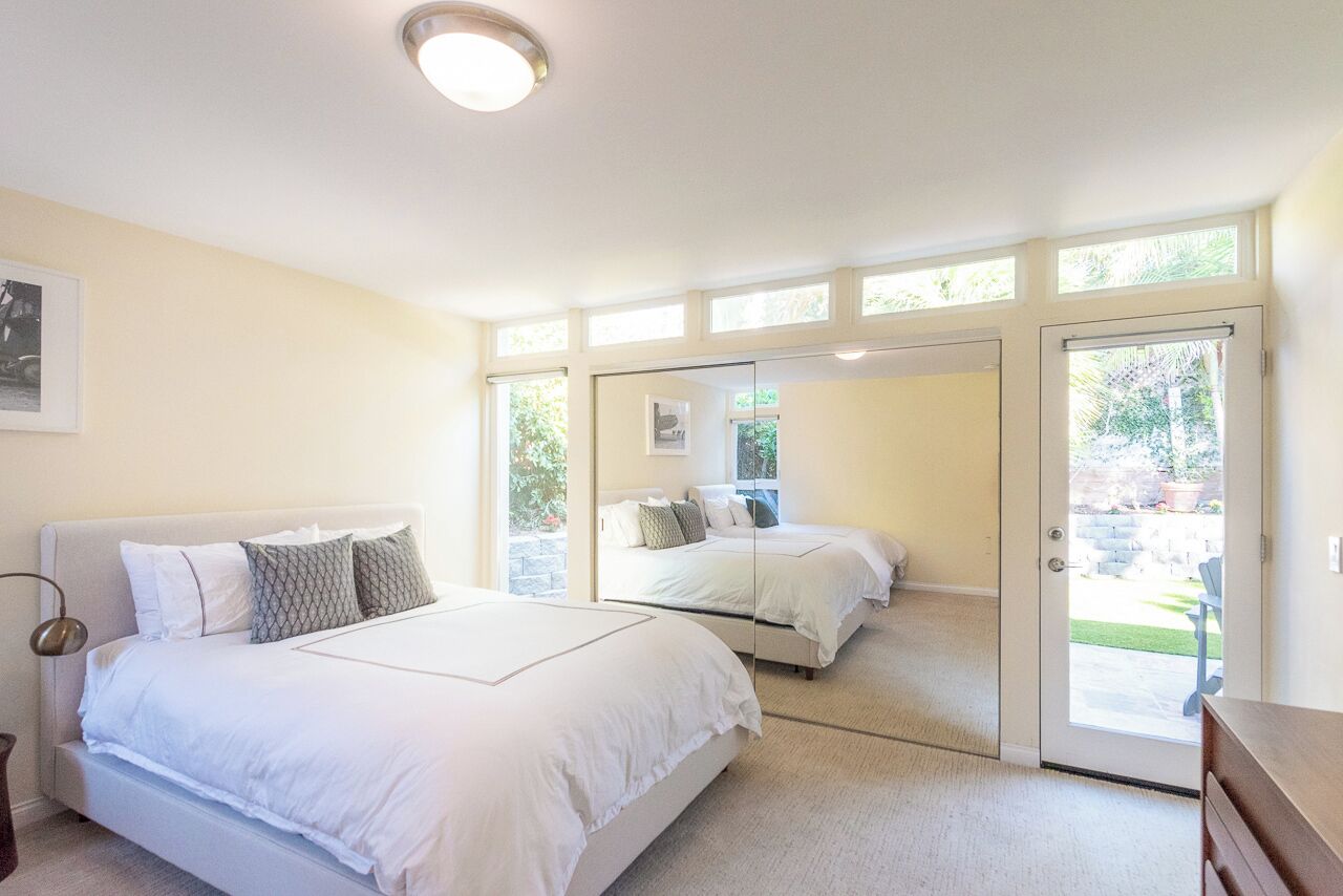 A bedroom with a large bed, a mirror, and a sliding glass door leading to a patio.