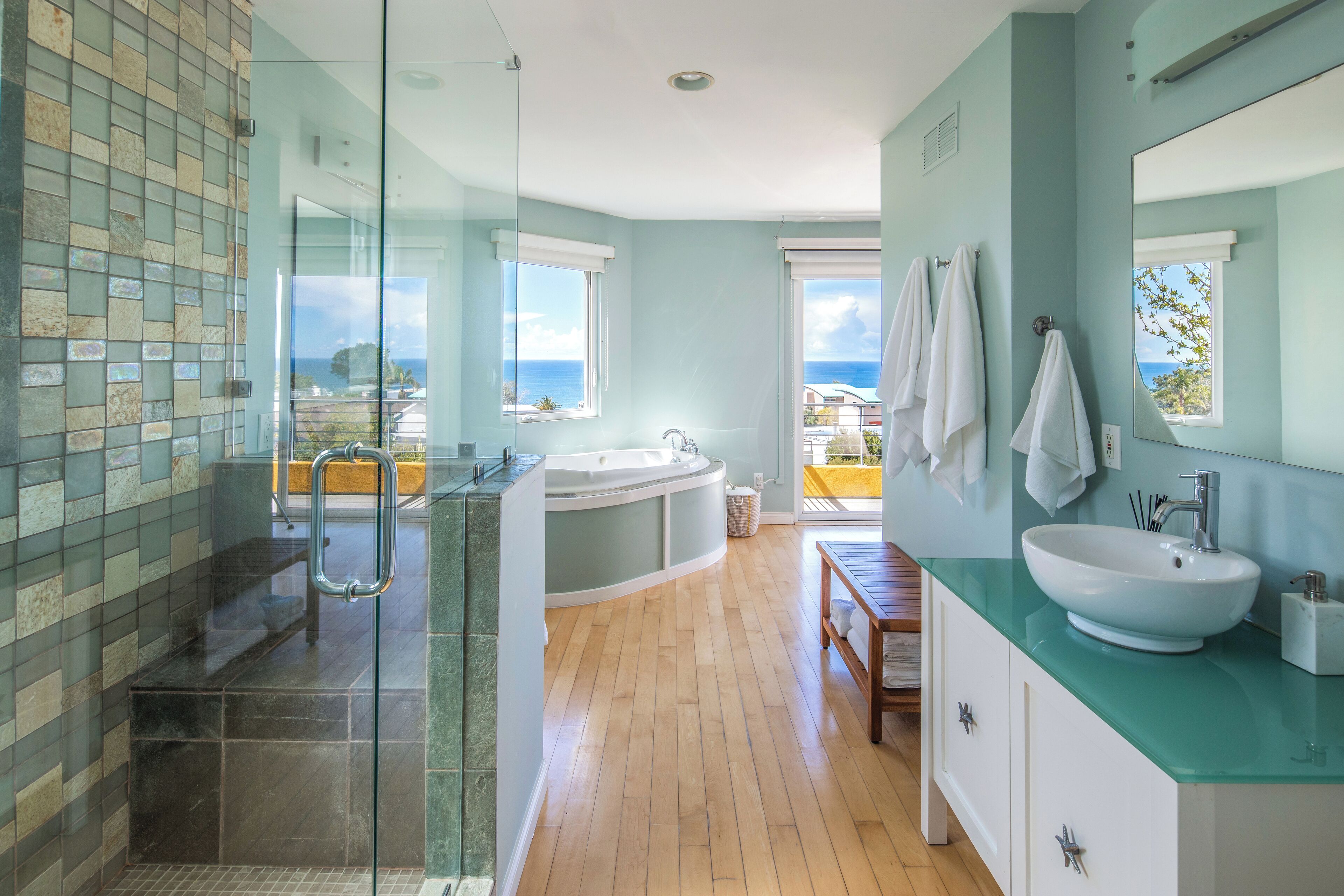 Une salle de bain moderne dotée d’une douche à parois de verre, d’une baignoire sur pied, d’un grand lavabo et offrant une vue sur l’océan.