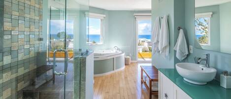 Une salle de bain moderne dotée d’une douche à parois de verre, d’une baignoire sur pied, d’un grand lavabo et offrant une vue sur l’océan.