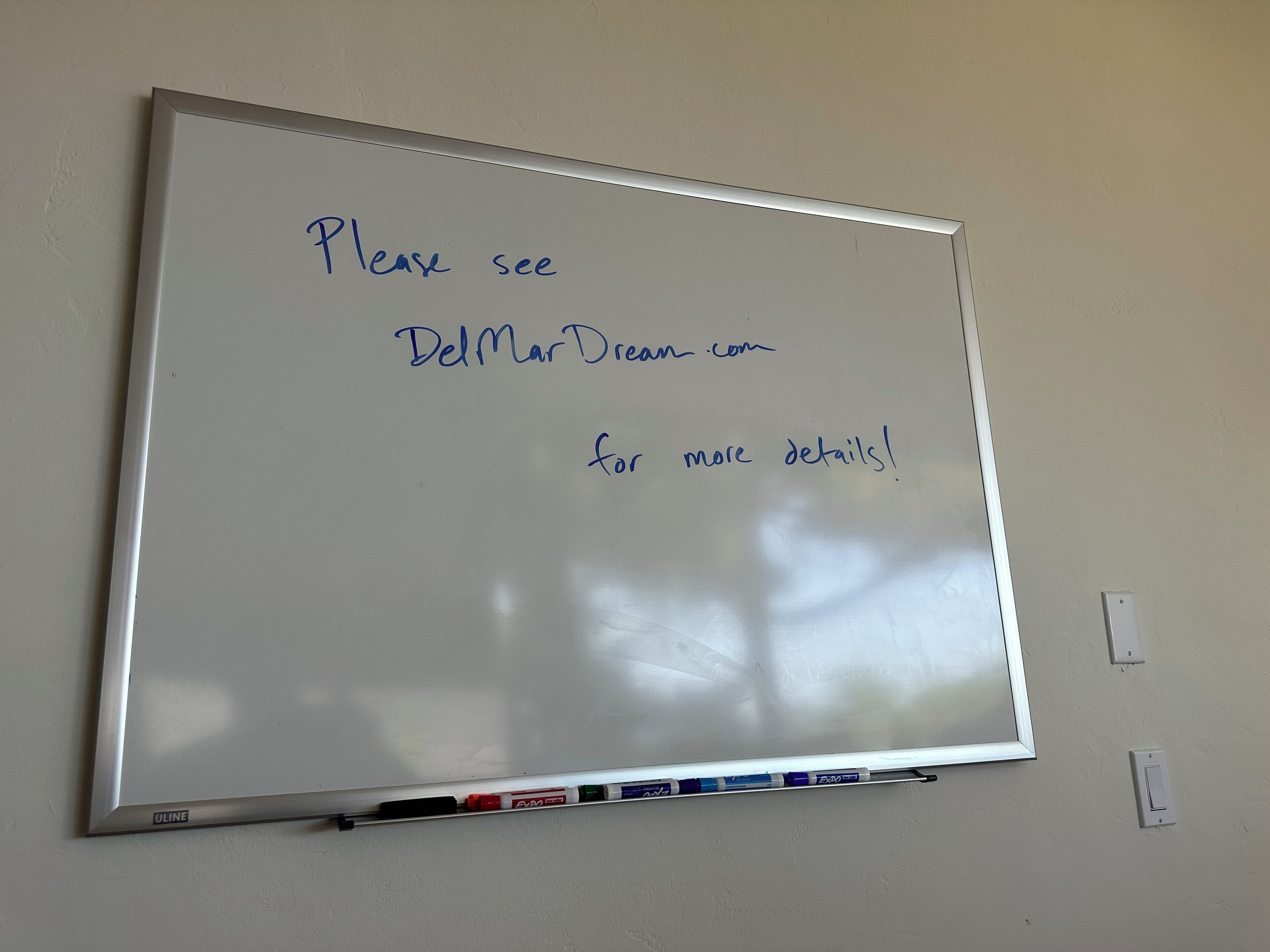 A whiteboard with handwritten text directing to a website for more details.