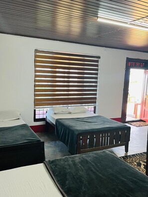 Ein Zimmer mit zwei Betten, einem Fenster mit Jalousien, einer Tür und einer roten Wand.